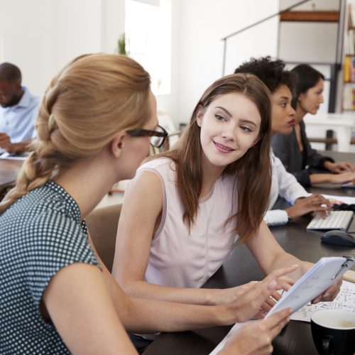 Woman training new female employee in an open plan office